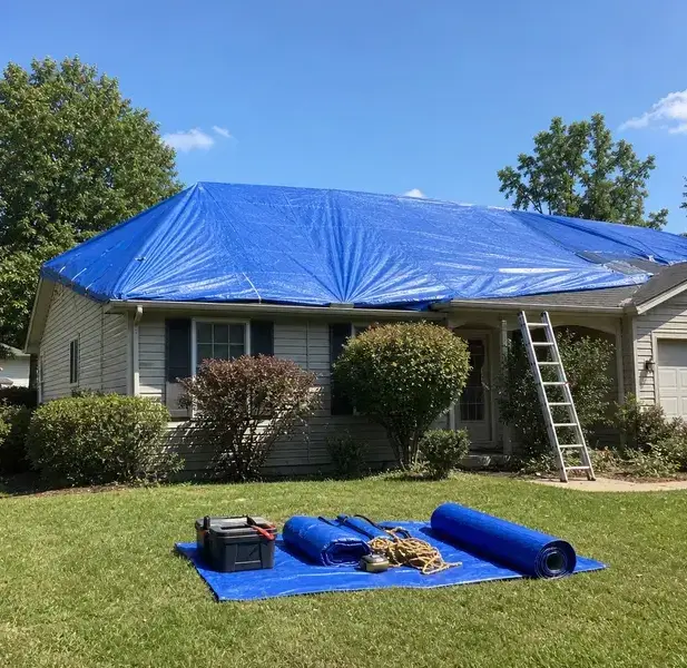 Blue roof tarp secured over a house with a ladder and spare tarps on the lawn in Peoria, AZ
